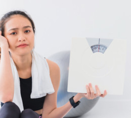 asian woman holding up a scale in frustration at not losing weight
