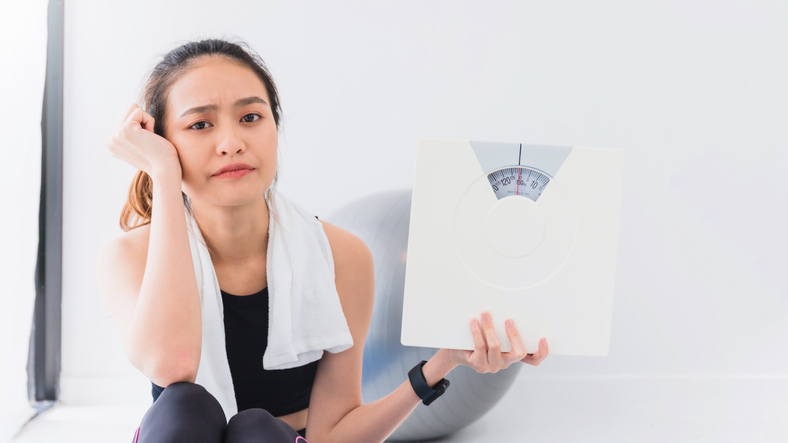 asian woman holding up a scale in frustration at not losing weight